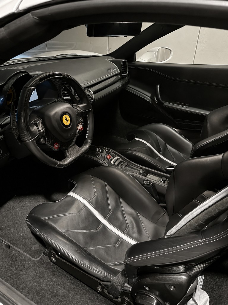 法拉利 458 Speciale 黑色真皮內裝與白色對比縫線、碳纖維飾板，座椅與方向盤呈自然霧面質感，象徵健康皮革狀態