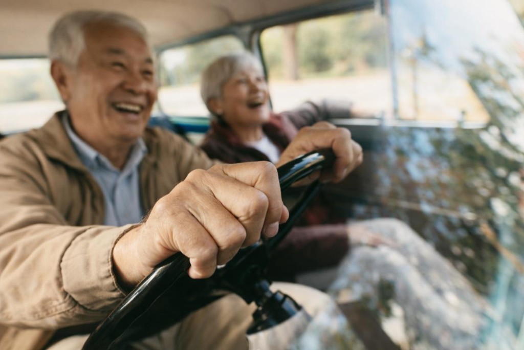 銀髮伴侶日間開車出遊，手握方向盤、車內溫馨笑語的休閒用車情境