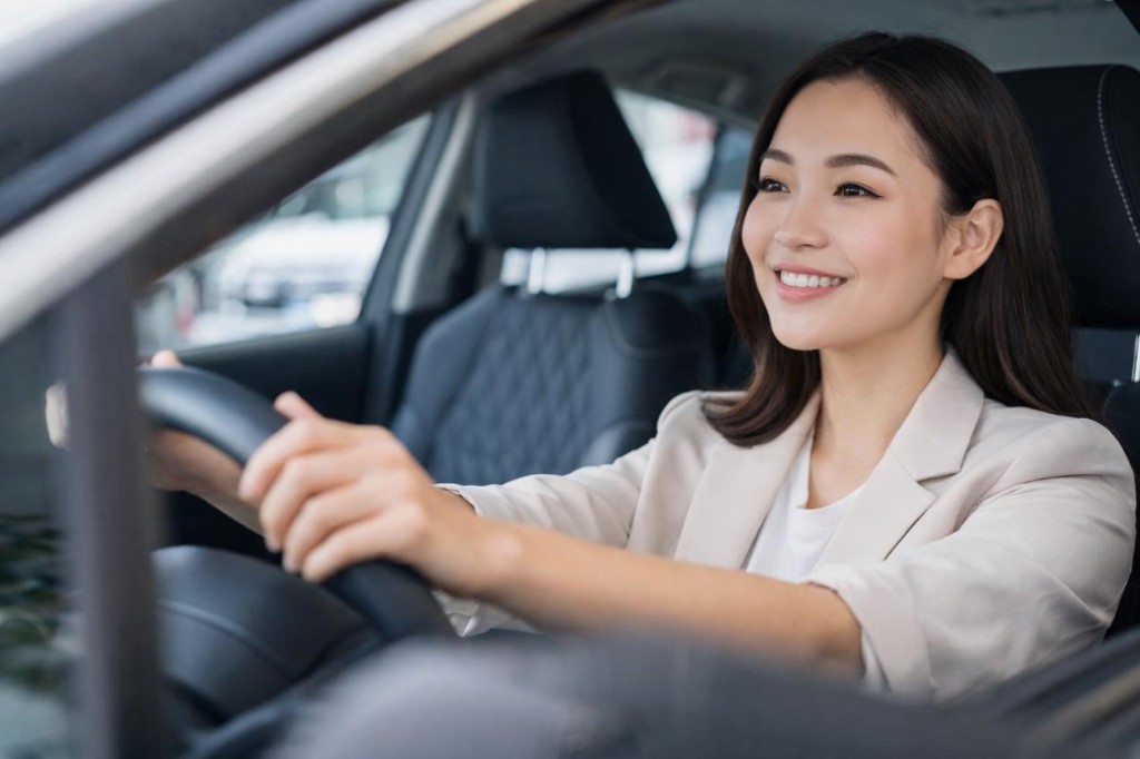 女性駕駛於現代車內雙手握持方向盤、微笑前行，象徵高頻通勤與對穩定用車的重視